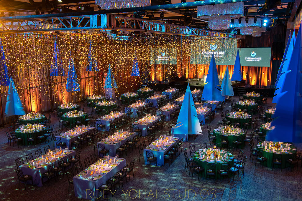 An elegant gala event setup organized by an event planning company, with decorated tables, blue lighting, and a ceiling draped with sparkling lights.