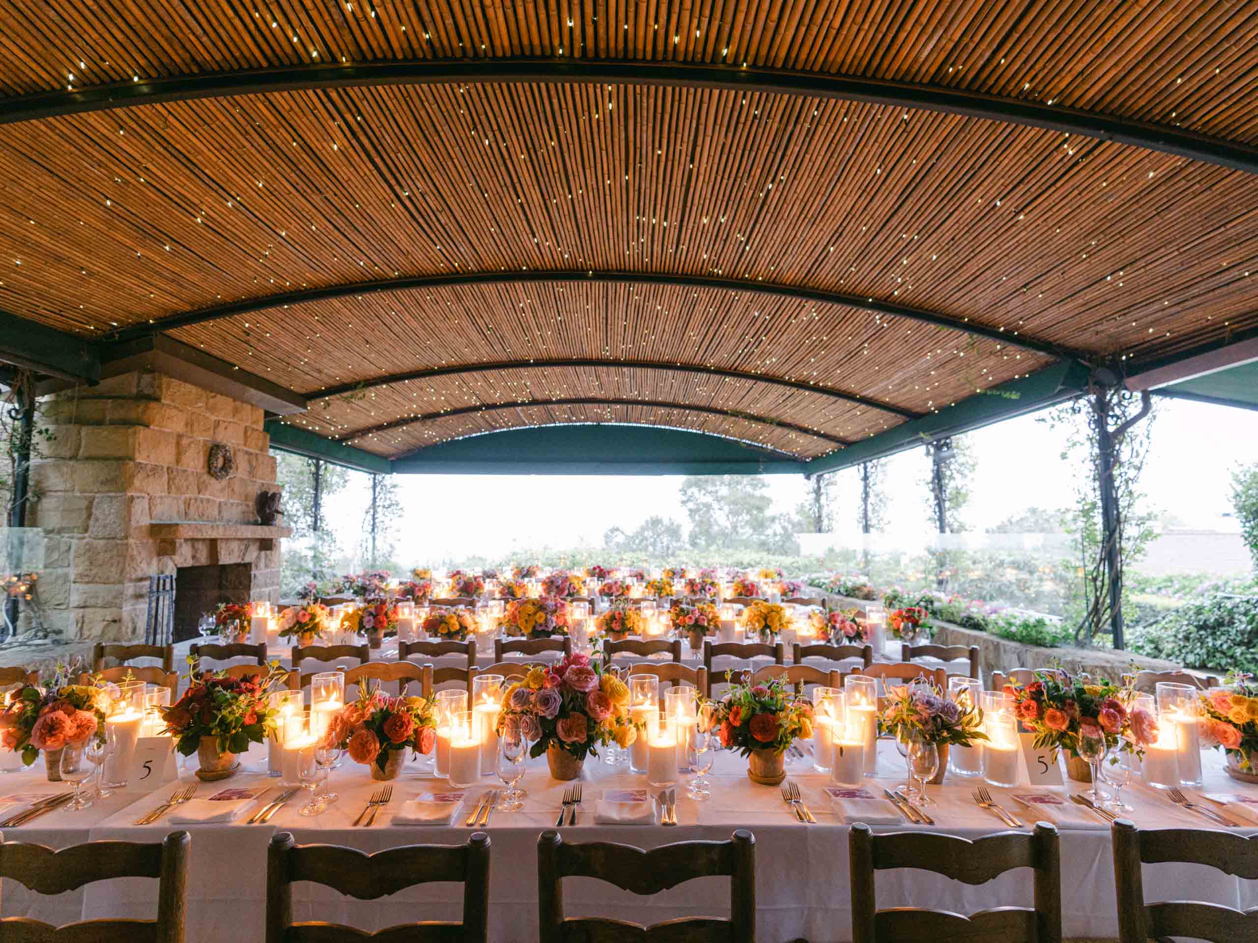 Elegant outdoor banquet setup with floral centerpieces and candle lighting under a curved wooden canopy, meticulously organized by a team of professional event planners.