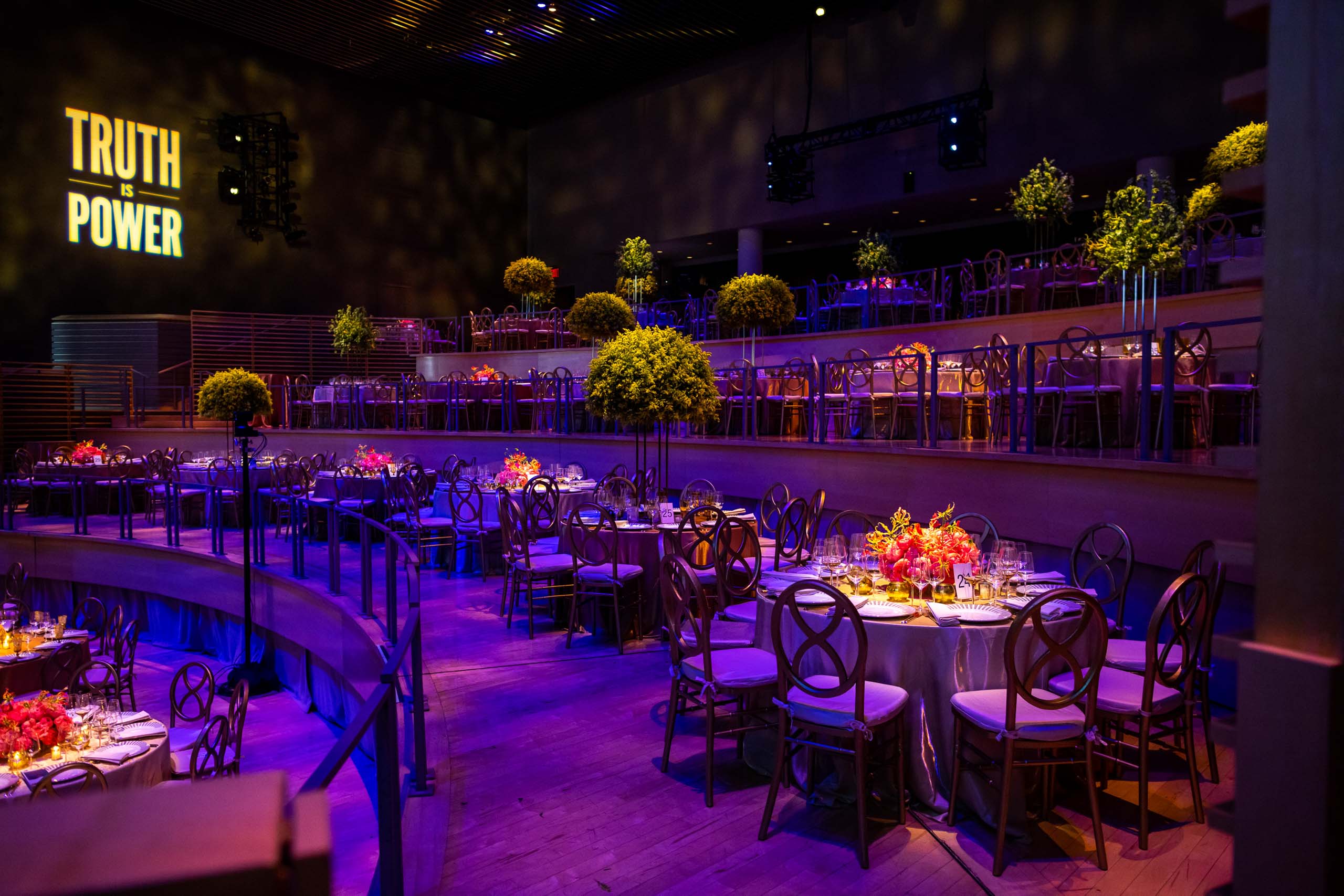 Elegant event venue space with dining tables set up for an occasion, atmospheric lighting, and a neon sign reading 'truth power' on the wall.