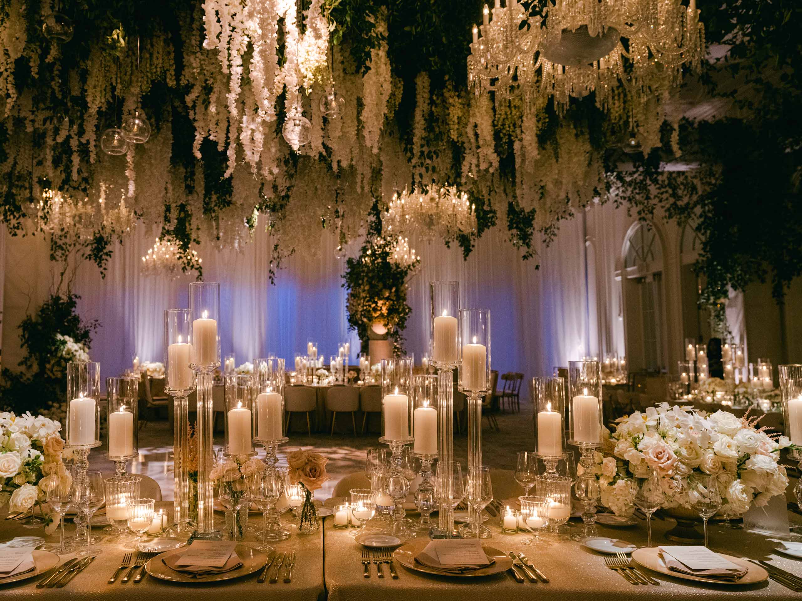 Elegant banquet hall adorned with chandeliers, hanging floral arrangements, and candlelit tables offered by a premier event planning company.